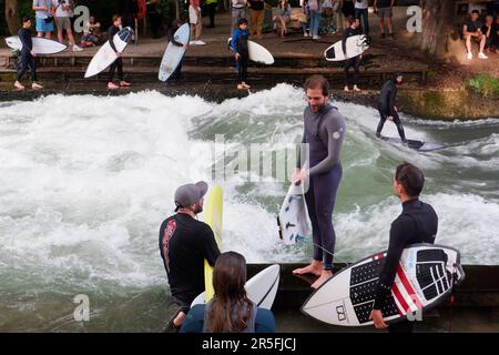 Surfisti all'onda artificiale di Eisbach sul fiume Isar che scorre attraverso il parco Englischer Garten (Giardini inglesi) a Monaco di Baviera in Germania Foto Stock