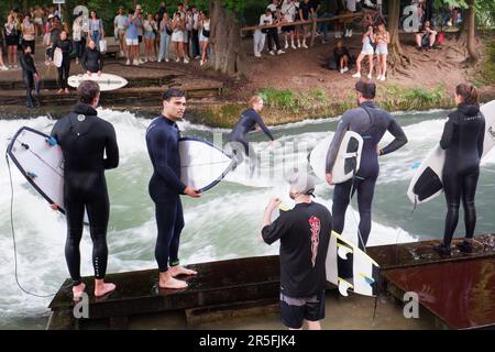 Surfisti all'onda artificiale di Eisbach sul fiume Isar che scorre attraverso il parco Englischer Garten (Giardini inglesi) a Monaco di Baviera in Germania Foto Stock