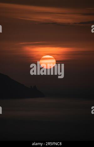 Tramonto con un grande sole rosso che si nasconde all'orizzonte sul mare e vicino alle scogliere di la Gomera dall'isola di Tenerife Foto Stock