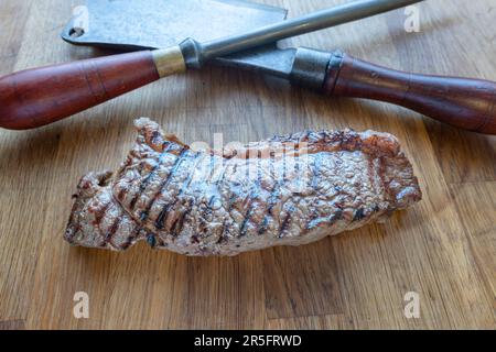Rustic Carne chopper accentua la presentazione di una bistecca alla griglia, affettata e servita su un asse di legno. Foto Stock