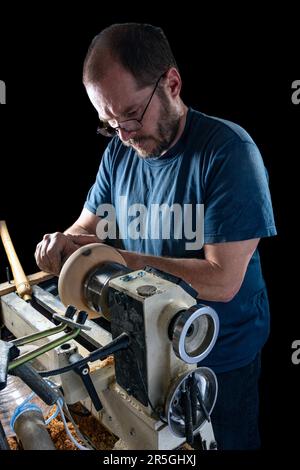 Artigiano che crea una ciotola di legno sul tornio. Immagine in officina. Sfondo nero. Foto Stock