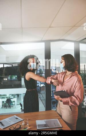 Le protuberanze del gomito sono la nuova normalità durante Covid. due donne d'affari in piedi insieme e si inchinano a vicenda e indossano maschere facciali durante una riunione Foto Stock