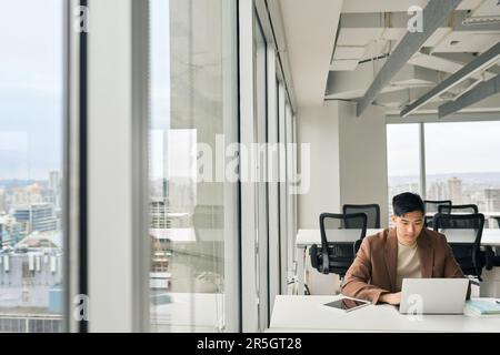 Giovane uomo d'affari asiatico che lavora su un computer portatile in un grande ufficio aziendale. Foto Stock