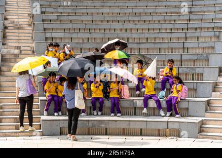 Un gruppo di scolari utilizza gli ombrelloni per Shelter from the Sun durante una visita all'Hong Kong Park, Hong Kong, Cina. Foto Stock