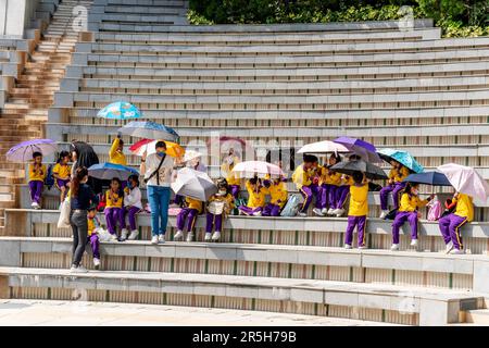 Un gruppo di scolari utilizza gli ombrelloni per Shelter from the Sun durante una visita all'Hong Kong Park, Hong Kong, Cina. Foto Stock