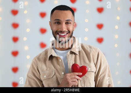 Bel giovane uomo con cuore di legno rosso all'interno, vista dalla macchina fotografica. Festa di San Valentino in rapporto a lunga distanza Foto Stock