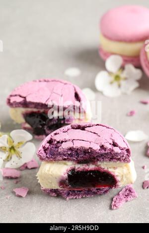 Metà di delizioso macaron viola e fiori su tavolo grigio chiaro Foto Stock