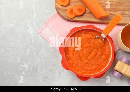 Alimenti sani per bambini. Ciotola con deliziosa purea di carote su tavolo in marmo grigio chiaro, piatto. Spazio per il testo Foto Stock