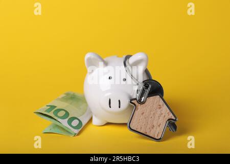 Banca di maialino in ceramica, banconota da euro e chiave con canestro su fondo giallo. Risparmi finanziari Foto Stock