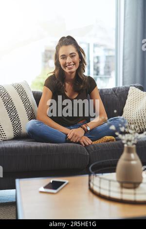 Ive ha tutto ciò di cui ho bisogno proprio qui a casa. Scatto integrale di una bella giovane donna che si rilassa sul suo divano a casa. Foto Stock