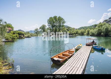 Barche accanto a un passaggio pedonale in legno nel villaggio di Karuc sul bordo del lago Skadar in Montenegro, nella foto nel maggio 2023. Foto Stock