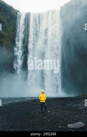 Scenografico scenario della cascata di Skogafoss che scorre con una donna asiatica in piedi in estate in Islanda Foto Stock