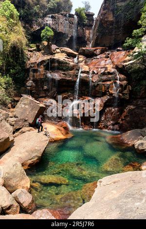 Donna escursionista in piedi su una roccia guardando la splendida cascata Prut con piscina naturale turchese nella regione di Cherrapunji a Meghalaya, India Foto Stock