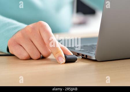 Primo piano delle mani di una donna che collega il caricabatterie a un notebook a casa Foto Stock