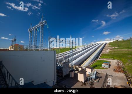 Tubazioni e torri elettriche della centrale idroelettrica e trasformatore (a sinistra) su sfondo blu cielo Foto Stock