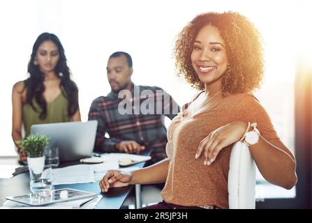 Condividere di più ci rende un team più forte. Ritratto di una giovane donna fiduciosa che ha un incontro con i suoi colleghi sullo sfondo. Foto Stock