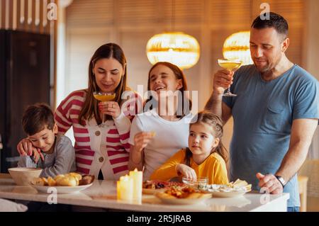 Grande famiglia felice sta pranzando nella sala da pranzo. Genitori e bambini si divertono a casa. Papà tiene un bicchiere di Chmpagne. Festa di famiglia. Adolescente Foto Stock