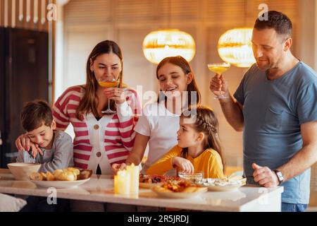 Grande famiglia felice sta pranzando nella sala da pranzo. Genitori e bambini si divertono a casa. Papà tiene un bicchiere di Chmpagne. Festa di famiglia. Adolescente Foto Stock