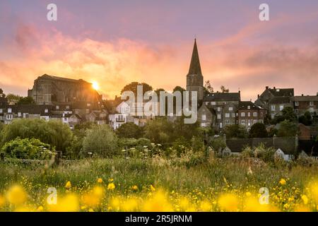 Domenica 4th giugno 2023. Malmesbury, Wiltshire, Inghilterra - le nuvole si sciolgono mentre il sole sorge dietro la storica abbazia e un prato di coppette Foto Stock