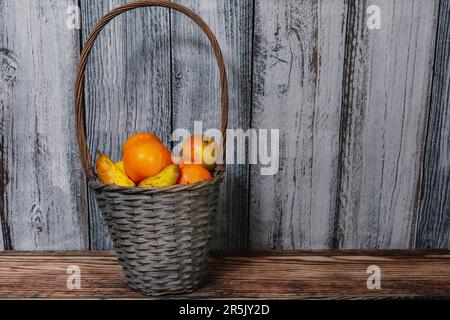 Un cesto di frutta contenente arance, mele e pere su sfondo di legno Foto Stock