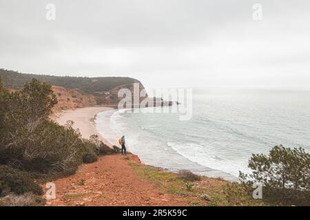 L'escursionista si trova sul bordo di una scogliera e guarda la spiaggia sotto chiamata Praia do Burgau sulla costa sud-occidentale del Portogallo nel turistico e famoso Foto Stock