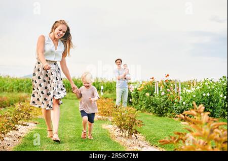 Famiglia giovane felice con la bambina ed il bambino che gioca insieme sulla fattoria dei fiori Foto Stock