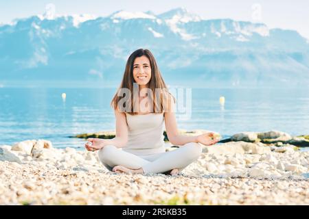 Bella donna spirituale meditando sul lago, indossando abiti beige Foto Stock