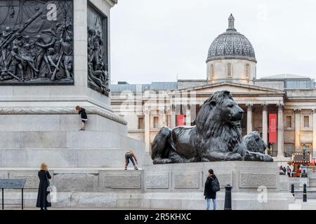 I bambini si arrampicano e giocano sulla base della colonna di Nelson a Trafalgar Square, Londra, Regno Unito Foto Stock