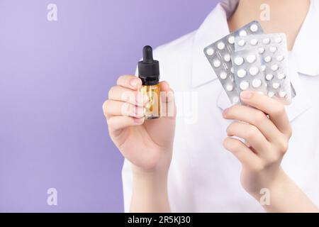 In una mano di una dottoressa ci sono bottiglie di estratto di olio di cbd, nell'altra mano ci sono diversi blister di compresse. Medico alternativo c Foto Stock