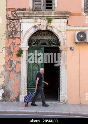 Sibenik, Croazia - 31 maggio 2023: Un uomo anziano che cammina dalla porta d'ingresso dell'arco mentre tira il carrello Foto Stock