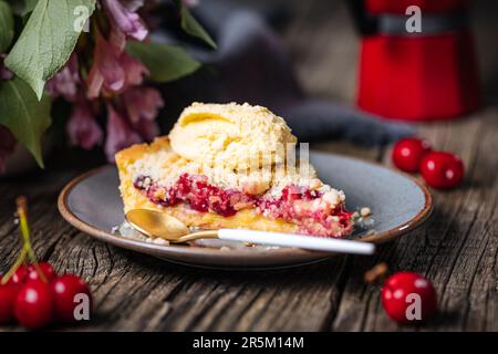 Crostata con crema di ciliegia acida, pasticceria creme e briciole, servita con gelato alla vaniglia. Atmosfera rustica e moody e decorazione. Foto Stock