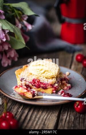 Crostata con crema di ciliegia acida, pasticceria creme e briciole, servita con gelato alla vaniglia. Atmosfera rustica e moody e decorazione. Foto Stock