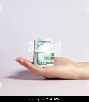 In mano si trova un pacchetto di dollari, arrotolato in un rotolo. Foto Stock