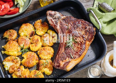 Bistecca di prima qualità con patate al forno servita nel vassoio di metallo Condite con rosmarino, pepe e aglio. Succulenta e deliziosa bistecca Ribeye Foto Stock