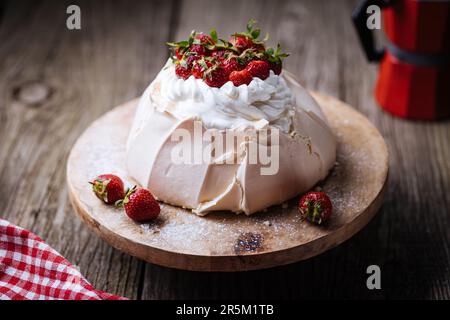 Pavlova torta decorata con fragole su rustico tavolo di legno. La torta è fatta di meringa e panna montata Foto Stock