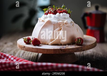 Pavlova torta decorata con fragole su rustico tavolo di legno. La torta è fatta di meringa e panna montata Foto Stock