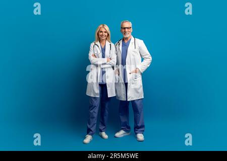 Medici anziani positivi in abbigliamento da lavoro medico in posa su blu Foto Stock