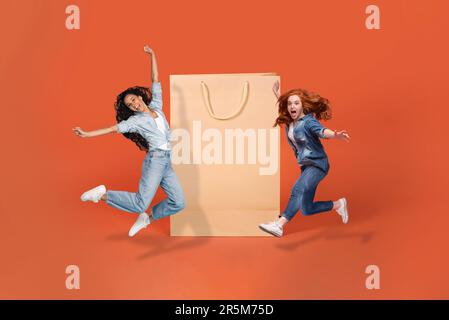 Buone ragazze che saltano accanto a una grande borsa per lo shopping Foto Stock