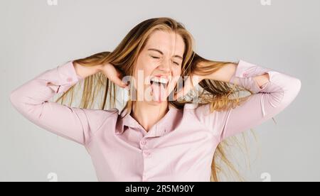 Ritratto di ragazza bionda divertente mostrando lingua. Donna felice con i capelli lunghi con gli occhi chiusi. Donna sorridente con capelli sporchi nelle mani. Modello femmina con Foto Stock