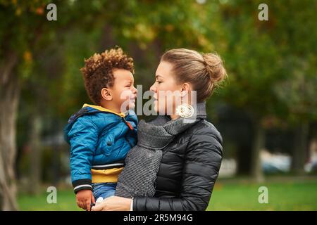 Giovane madre che tiene piangere bambino, genitore nel parco con bambino triste, mix razza famiglia Foto Stock