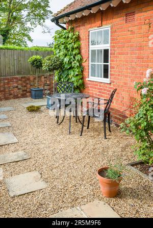 UK giardino patio design. Terreno duro con pietre di York passo in pietra in ghiaia e un tavolo da bistrot in metallo e sedie. Foto Stock