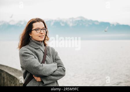 Ritratto all'aperto di bella donna, vestito di grigio, in posa accanto al lago Foto Stock