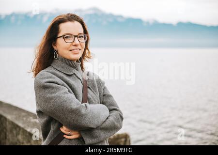 Ritratto all'aperto di bella donna, vestito di grigio, in posa accanto al lago Foto Stock