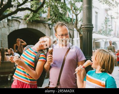 Buon padre con i bambini che mangiano gelato all'aperto, tempo della famiglia, viaggi con i bambini Foto Stock