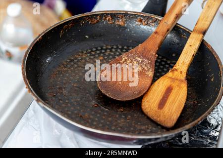 Teglia di ghisa rotonda nera vuota con una spatola e una spatola di legno che aveva appena finito di cucinare sulla stufa a metà giornata Foto Stock