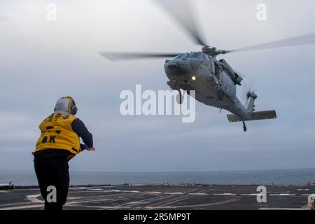 230423-N-EU502-3202 OCEANO PACIFICO (23 aprile 2023) - il compagno di Boatswain Seaman Edwin Falcon-Fernandez, di Boston, dirige un elicottero MH-60R Sea Hawk assegnato all'elicottero Maritime Strike Squadron (HSM) 71 mentre atterra sul ponte di volo dell'incrociatore missilistico guidato USS Mobile Bay (CG 53), 23 aprile 2023. Mobile Bay è in corso con la Carl Vinson Carrier Strike Group conducing Group Sail, che dimostra la capacità di aggregare rapidamente le unità del gruppo sciopero e offre l'opportunità di condurre corsi di formazione per migliorare i livelli di eccellenza e aumentare la letalità e il profico tattico Foto Stock