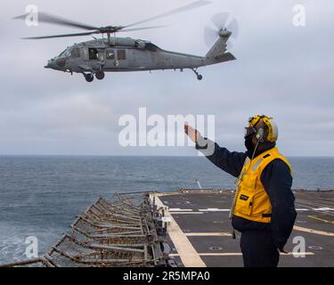 230423-N-EU502-3258 OCEANO PACIFICO (23 aprile 2023) - Boatswain’s Mate 2nd Class Ronald “Goody” Goodwin, di Filadelfia, dirige un elicottero MH-60R Sea Hawk assegnato all'elicottero Maritime Strike Squadron (HSM) 71 mentre parte dal ponte di volo dell'incrociatore missilistico guidato USS Mobile Bay (CG 53), 23 aprile 2023. Mobile Bay è in corso con la Carl Vinson Carrier Strike Group conducing Group Sail, che dimostra la capacità di aggregare rapidamente le unità del gruppo sciopero e offre l'opportunità di condurre corsi di formazione per migliorare i livelli di eccellenza e aumentare la letalità e la tattica Foto Stock