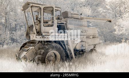 Una vecchia mietitrebbia Massey Ferguson 760 abbandonata ai margini di un campo, accanto ad alcuni alberi, scattata in 720nm colori falsi a infrarossi. Foto Stock