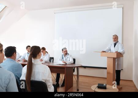 Dottore senior che tiene lezioni in sala conferenze con schermo di proiezione Foto Stock