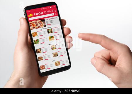 Servizio di consegna cibo. Uomo scegliendo piatto dal menu sul posto utilizzando smartphone su sfondo bianco, primo piano Foto Stock